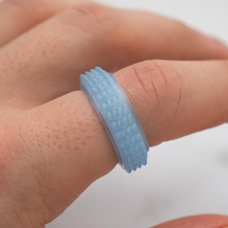 May include: A light blue ring with a textured surface. The ring has a series of small, raised rectangular patterns around the band. The ring is on a finger.