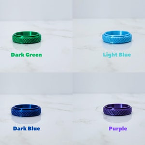 May include: Four different colored rings with a textured surface. The rings are dark green, light blue, dark blue, and purple.