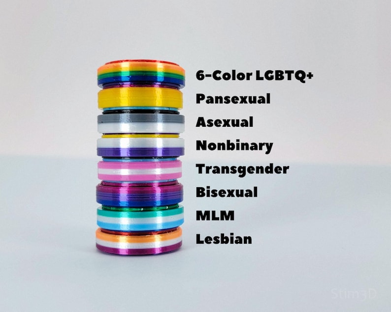 Puede incluir: Una pila de anillos coloridos con diferentes dise&ntilde;os de banderas del arco&iacute;ris. Los anillos est&aacute;n etiquetados con las siguientes identidades: 6-Color LGBTQ+, Pansexual, Asexual, No binario, Transg&eacute;nero, Bisexual, MLM, Lesbiana.