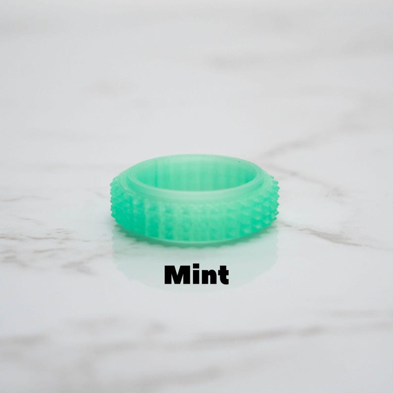 May include: A mint-colored ring with a textured, studded exterior. The ring is a solid, circular band with a slightly raised center. The word "Mint" is printed in black, centered below the ring.