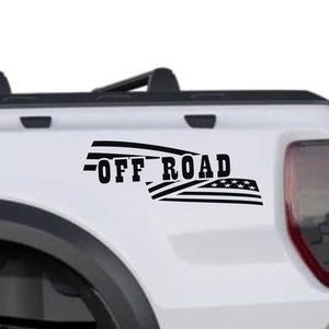 Op de afbeelding: Een witte pick-up truck met een zwarte "OFF ROAD" sticker met een Amerikaans vlagontwerp op de achterklep.