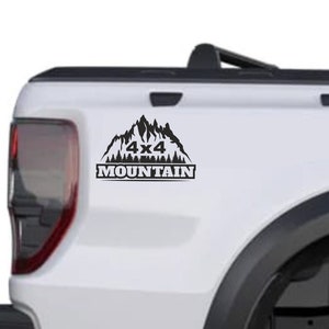 Può includere: Un pick-up bianco con un adesivo nero 4x4 Mountain sul portellone. Il camion ha un pneumatico nero e un cerchio nero.