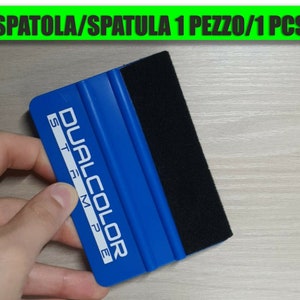 Può includere: Spatola in plastica blu con bordo in feltro nero. La spatola ha la scritta "DUAL COLOR ST-MPE" stampata.