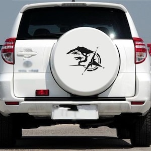 Könnte beinhalten: Ein weißer SUV mit einer Reserveradabdeckung, die eine schwarze Silhouette eines Baumes und einen Kompass zeigt. Der Kompass zeigt nach Norden, Süden, Osten und Westen.