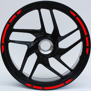 Op de afbeelding: Zwarte motorfiets velg met rode accentstrepen en zwarte stippen.