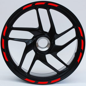 Peut inclure: Une jante de roue de moto noire avec des bandes décoratives rouges autour du bord.