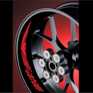 Könnte beinhalten: Eine schwarze Motorrad-Felge mit roten Rennstreifen. Das Rad hat sechs Speichen und eine schwarze Mitte mit weißen Schrauben.