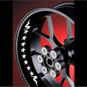 Op de afbeelding: Een zwarte motorfietsvelgen met een wit sterren- en silhouetontwerp. Het wiel heeft een rode achtergrond.