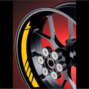 Op de afbeelding: Een zwarte motorfietsvelgen met een gele streep en pijlontwerp. Het wiel heeft zes witte spaken en een zwarte naafdop.