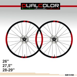 Può includere: Una coppia di ruote da bicicletta nere con strisce rosse e nere. Le ruote sono di 26", 27,5" e 28-29". DUALCOLOR STAMP è scritto in rosso e verde nella parte superiore dell'immagine. Il testo "made in Italy" è nella parte inferiore dell'immagine.