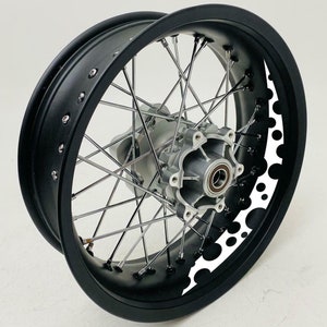 Op de afbeelding: Zwart motorfietswiel met een witte velgstreep en een cirkelpatroon. Het wiel heeft zilveren spaken en een zilveren naaf.