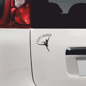Op de afbeelding: Een witte auto met een zwart silhouet van een ballerina en de tekst "I LOVE DANCE" op de achterkant.