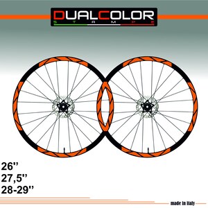 Può includere: Due ruote di bicicletta con cerchi neri e dettagli arancioni. Le ruote hanno raggi argentati e un freno a disco centrale. Il testo "DUALCOLOR STAMPE" è in alto, con le misure 26", 27,5" e 28-29" sotto. Prodotto in Italia.