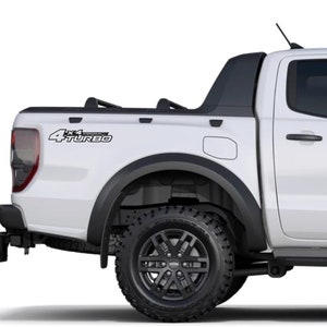 Può includere: Un pick-up Ford Ranger bianco con una copertura del cassone nera e ruote nere. Il pick-up ha un adesivo "4x4 Turbo" sul lato del cassone.