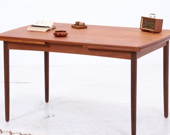 Könnte beinhalten: Ein Esstisch aus Holz im Mid-Century-Modern-Stil mit rechteckiger Tischplatte und vier konischen Beinen. Der Tisch hat eine warme braune Farbe und eine Blattausziehbar. Eine kleine Uhr, eine Schale und ein Buch liegen auf dem Tisch.