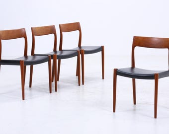 Könnte beinhalten: Vier Esszimmerstühle im Mid-Century-Modern-Stil. Die Stühle haben ein Holzgestell mit dunklem Finish und einen schwarzen Sitz. Die Stühle sind in einer Gruppe von drei und einem vor einem weißen Hintergrund angeordnet. Die Stühle sind ein klassisches Design.