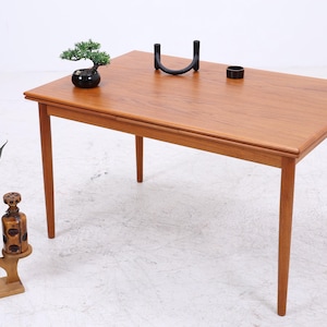 Peut inclure: Table rectangulaire en bois clair avec quatre pieds. Sur le dessus, un petit bonsaï dans un pot noir, un bougeoir noir et un anneau noir. Un support de plante décoratif avec une plante en pot et une bouteille décorative sont à gauche.