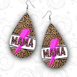 May include: A pair of dangle earrings with a leopard print design. The earrings are shaped like a teardrop and feature a pink lightning bolt with the word "MAMA" written in white letters.