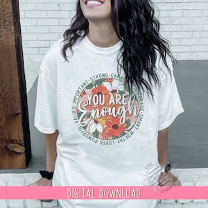 K&ouml;nnte beinhalten: Ein wei&szlig;es T-Shirt mit einem gr&uuml;nen Kreisdesign, das ein Blumenmuster und den Text "You Are Enough" zeigt. Der Kreis ist von W&ouml;rtern wie "wichtig", "stark", "f&auml;hig", "mutig", "klug", "w&uuml;rdig", "geliebt", "m&auml;chtig", "gesch&auml;tzt" umgeben.