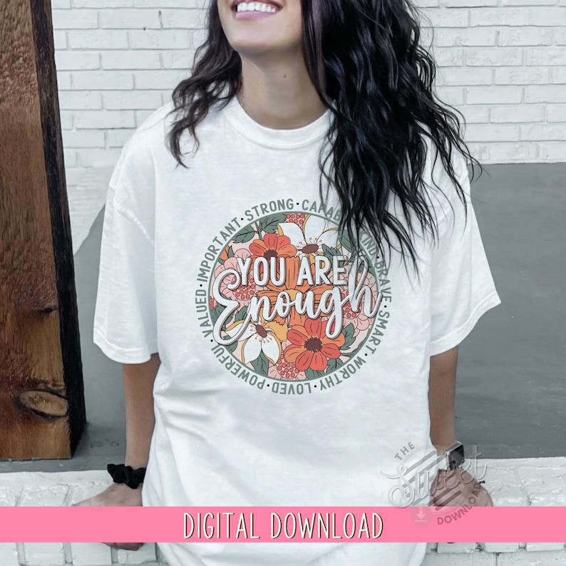 K&ouml;nnte beinhalten: Ein wei&szlig;es T-Shirt mit einem gr&uuml;nen Kreisdesign, das ein Blumenmuster und den Text "You Are Enough" zeigt. Der Kreis ist von W&ouml;rtern wie "wichtig", "stark", "f&auml;hig", "mutig", "klug", "w&uuml;rdig", "geliebt", "m&auml;chtig", "gesch&auml;tzt" umgeben.