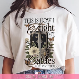 May include: Cream-colored t-shirt featuring the text "THIS IS HOW I Fight MY Battles" with a sword, shield, and Bible graphic. The design includes butterflies and floral elements, with the scripture reference Ephesians 6:10-18.