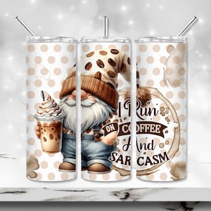 May include: Three stainless steel tumblers with a white background and brown polka dots. The centre tumbler features a cartoon gnome holding a coffee drink. The right tumbler has a coffee stain with the text "I Run on Coffee and Sarcasm".