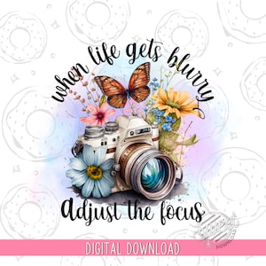 Puede incluir: Una ilustración de acuarela de una cámara vintage con una mariposa y flores. El texto "when life gets blurry adjust the focus" está escrito alrededor de la cámara.