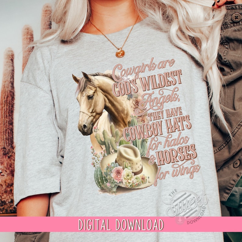 May include: A gray t-shirt with a graphic design of a horse, cactus, and a cowboy hat. The text on the shirt reads "Cowgirls are God's Wildest Angels. They have Cowboy Hats for halos & Horses for wings."
