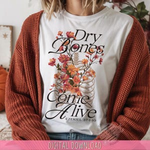 May include: White t-shirt with a floral rib cage design and the words "Dry Bones Come Alive" in black script. The design includes orange and red flowers. The text "Ezekiel 37:1-10" is below the main text.