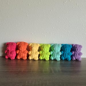 May include: A row of seven crocheted teddy bears in rainbow colours, from red to purple.