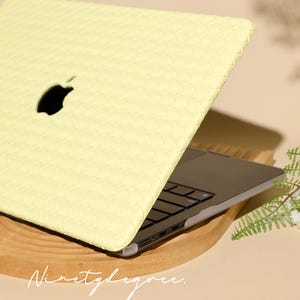 May include: A pale yellow laptop case with a woven texture pattern covering the exterior lid. The case features a cutout for the Apple logo and is fitted onto a dark grey laptop with black keys. The text Ninetydegree is visible at the bottom.