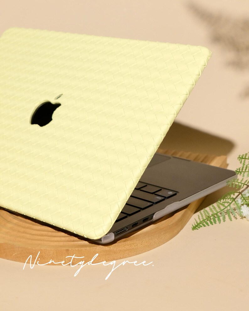 May include: A pale yellow laptop case with a woven texture pattern covering the exterior lid. The case features a cutout for the Apple logo and is fitted onto a dark grey laptop with black keys. The text Ninetydegree is visible at the bottom.