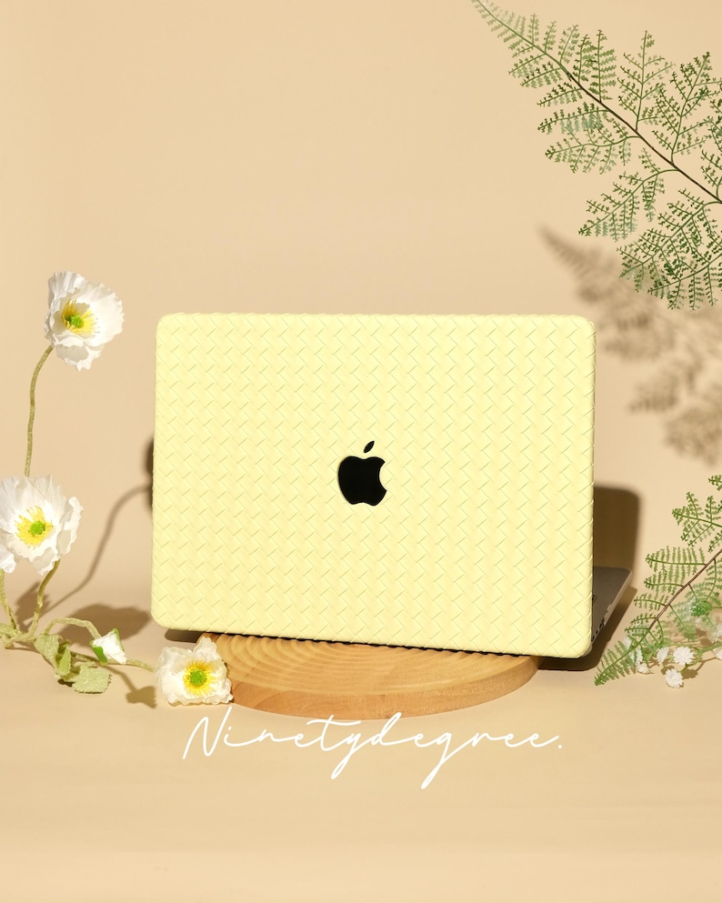 May include: A pale yellow laptop case with a woven texture pattern covering the exterior surface. The case features a central cutout revealing a black Apple logo. The text "Ninetydegree." is printed in white script at the bottom of the image.