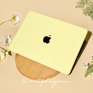 May include: A pale yellow laptop case with a woven texture pattern covering the exterior surface. The case features a central cutout revealing the black Apple logo. The text Ninetydegree is printed in a white script font below the laptop.