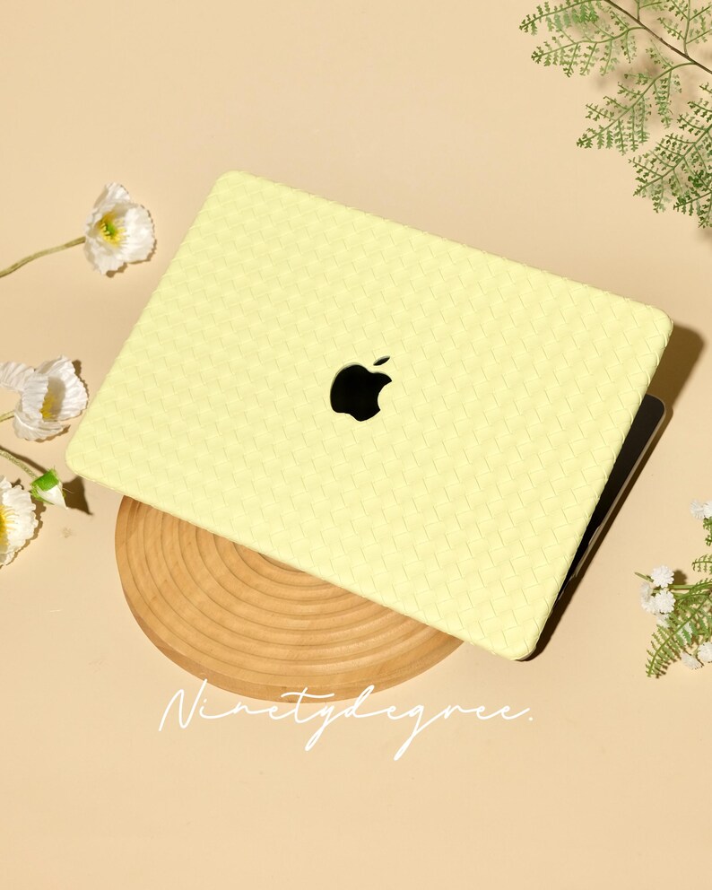 May include: A pale yellow laptop case with a woven texture pattern covering the exterior surface. The case features a central cutout revealing the black Apple logo. The text Ninetydegree is printed in a white script font below the laptop.