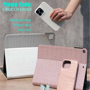 May include: Three phone cases with a crocodile pattern. The cases are in white, pink, and light pink. The white case is for a tablet, the pink case is for a phone, and the light pink case is for a phone. The text "Promo Code: CROCOSERIES" is at the top of the image. The text "MacBook case, iPhone case, iPad case" is below the cases.