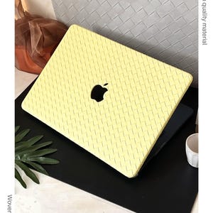 May include: A pale yellow laptop case featuring a textured, woven-style pattern across the entire surface. The case includes a central cutout revealing the black Apple logo. The text on the image reads Chic colour, High quality material, Woven style, and Perfectly fits your device.