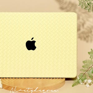 May include: A pale yellow laptop cover featuring a woven, basket-weave texture across the entire surface. A black Apple logo is centred on the cover. The text "Ninetydegree." is printed in a white, cursive script at the bottom of the cover.