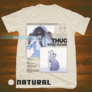 以下が含まれることがあります： ベージュのTシャツに、ヤング・サグのグラフィックプリントが施されています。グラフィックには、青と白の衣装を着たヤング・サグのポートレートと、「ヤング・サグ ジェフェリー（ミックステープ）」というテキスト、アルバムに関するその他の詳細が描かれています。Tシャツには、下部に「ナチュラル」という文字もプリントされています。