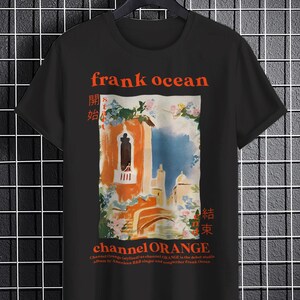 May include: Black t-shirt with a graphic print of a building with a balcony and flowers. The text "frank ocean" is printed in red above the graphic. The text "channel ORANGE" is printed in red below the graphic. The text "開始" and "結束" are printed in red on the left and right sides of the graphic, respectively.