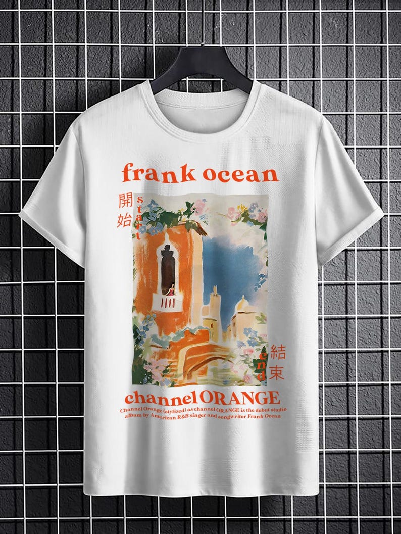 May include: White t-shirt with a graphic print of a painting of a building with a blue sky and flowers. The text "frank ocean" is printed in orange above the painting. The text "channel ORANGE" is printed in orange below the painting. The text "開始" and "結束" are printed in black on either side of the painting.