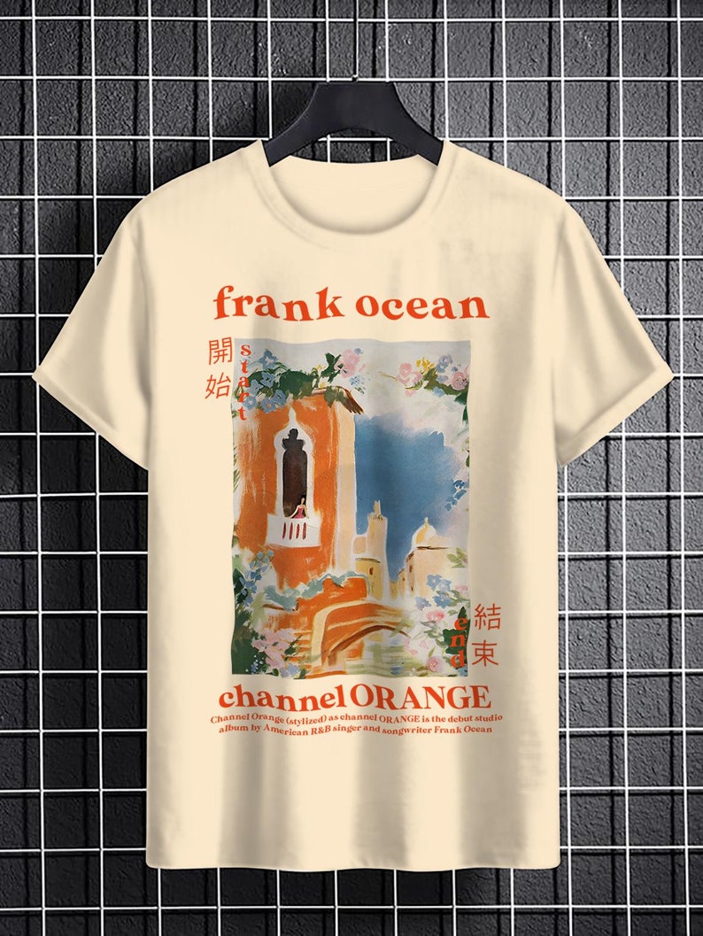 May include: A beige t-shirt with a graphic print of a building with a balcony and flowers. The text "frank ocean" is printed in red above the graphic. The text "channel ORANGE" is printed in red below the graphic. The text "開始" and "結束" are printed in black on either side of the graphic.