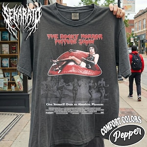 Op de afbeelding: Een antracietgrijs t-shirt met korte mouwen en een grafische print van The Rocky Horror Picture Show. Het ontwerp bevat rode lippen, een centraal figuur en kleinere figuren eronder met de tekst Give Yourself Over to Absolute Pleasure.