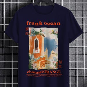 May include: A navy blue t-shirt with a graphic print of a building with a balcony and flowers. The text "frank ocean" and "channel ORANGE" is printed in red on the shirt. The text "開始" and "結束" is printed in red on the shirt in Japanese characters.