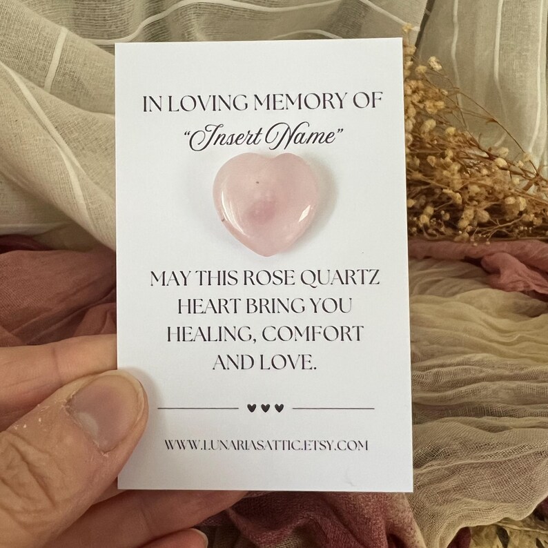 Op de afbeelding: Een roze rozenkwarts hart op een witte kaart. De kaart leest "IN LOVING MEMORY OF 'Insert Name'" en "MAY THIS ROSE QUARTZ HEART BRING YOU HEALING, COMFORT AND LOVE."