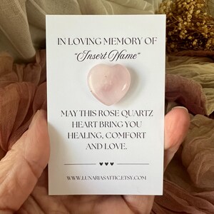 Op de afbeelding: Een rozenkwarts hartvormige steen op een witte kaart. De kaart leest "In Loving Memory Of" en "Insert Name". Hieronder staat "May this rose quartz heart bring you healing, comfort, and love."