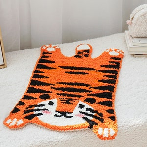 May include: Orange and black tiger rug with a cute face. The rug is made of fluffy yarn and has a textured surface.