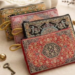 May include: Four rectangular zippered pouches featuring intricate woven patterns reminiscent of traditional rugs. Each pouch displays a unique color palette including red, black, pink, and green, and includes a gold cord loop attached to the zipper.