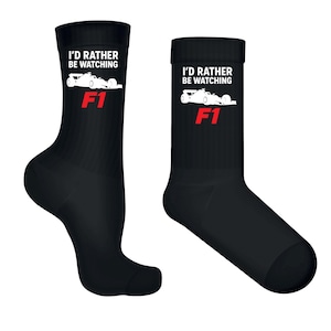 May include: Pair of black crew socks with the text "I'D RATHER BE WATCHING" above a white race car graphic and the red text "F1". The socks are made of a soft, comfortable material.