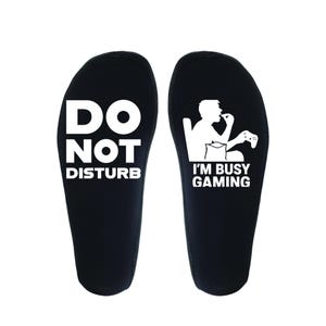 May include: Black insoles with white text. One insole reads "DO NOT DISTURB", the other reads "I'M BUSY GAMING" with a graphic of a person playing a video game. These insoles are designed for gamers.